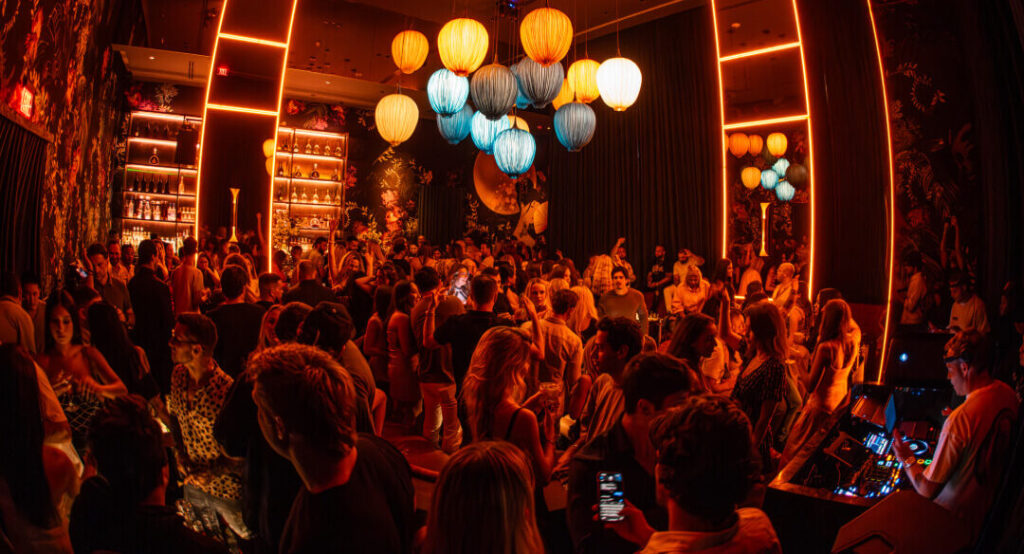 Vibrant nightlife scene at Gekko lounge with guests mingling under colorful lighting, floral wall murals, and glowing lanterns, creating an energetic and upscale party atmosphere.