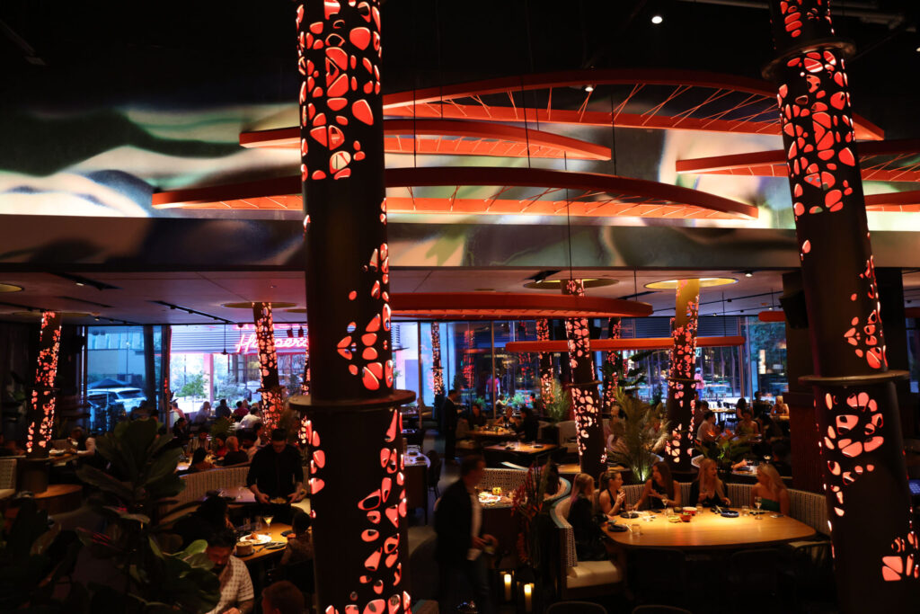 Evening dining at Komodo Miami with guests seated across multiple levels surrounded by glowing red bamboo columns