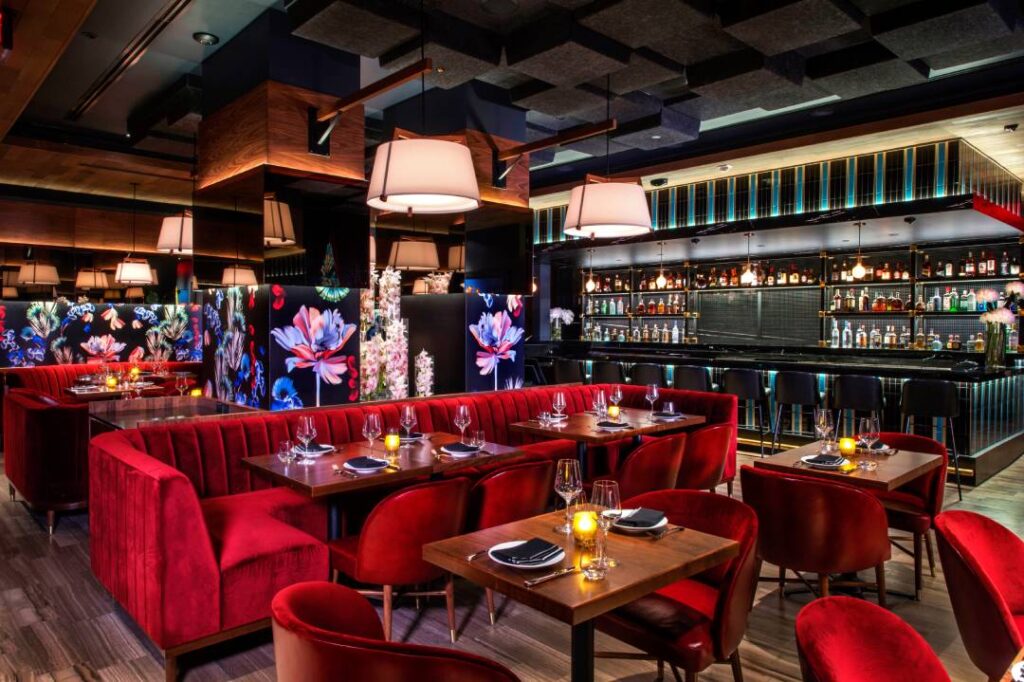 Papi Steak Miami interior featuring red velvet seating, floral wall art, elegant table settings, and a sleek black bar.