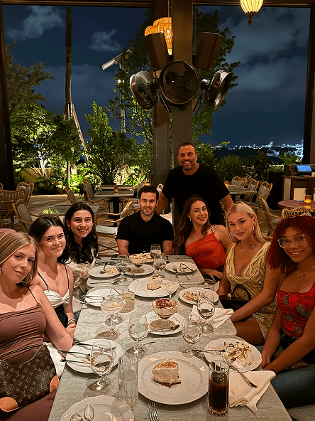 Groot Team dining outdoors at night, smiling around a table with desserts and drinks under ambient lighting.